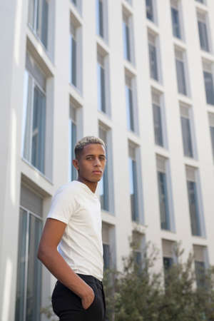 From below of African American male in elegant white shirt looking at camera while standing against modern skyscrapers in city on summer dayの写真素材