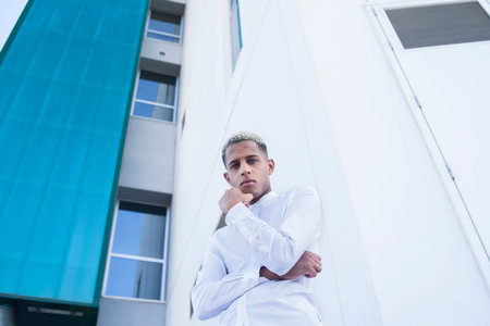 From below of African American male in elegant white shirt looking at camera while standing against...