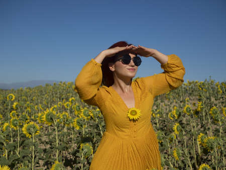 Delighted female with flying hair looking at camera with smile while holding yellow sunflower in field on summer day in countrysideの写真素材