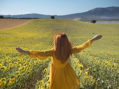 Delighted female with flying hair looking at camera with smile while holding yellow sunflower in...