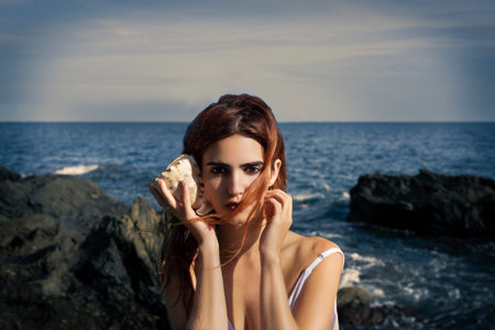 Full body of gorgeous young barefooted female in summer white maxi dress standing on rocky formation...