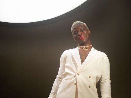 Glad androgynous African American man with short blond hair and red lips looking at camera with...