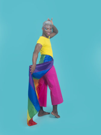Full body happy African American man with LGBT flag wrapped around hips touching head and looking at...
