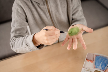 Boy painting his hands with watercolor with a brush with green colour
