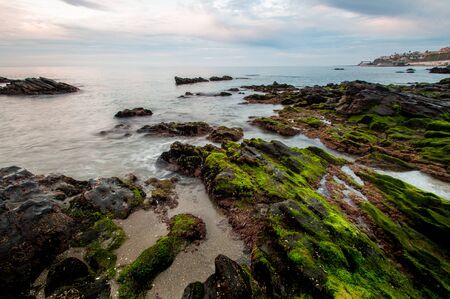 Impressive sunrise in a beach of Malaga, Andalusia with long exposure water and green rocks in firts placeの写真素材