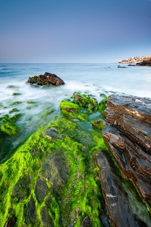 Impressive sunrise in a beach of Malaga, Andalusia with long exposure water and green rocks in firts placeの写真素材