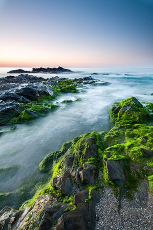 Impressive sunrise in a beach of Malaga, Andalusia with long exposure water and green rocks in firts placeの写真素材