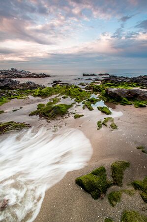 Impressive sunrise in a beach of Malaga, Andalusia with long exposure water and green rocks in firts placeの写真素材