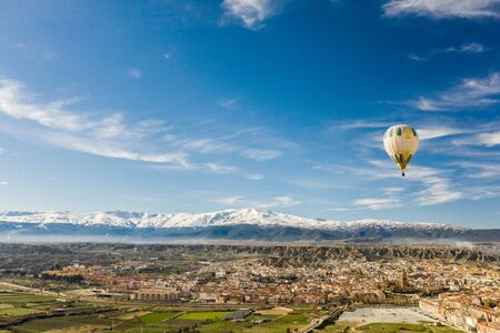 hot air balloon flying over Guadix one February morning with Sierra Nevada in the backgroundの写真素材
