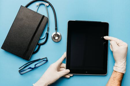 view of a doctors hands explaining the diagnosis of coronavirus with his tablet on his desk surrounded by medical materialの写真素材