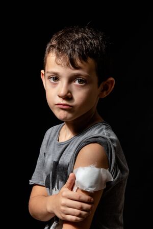 Cute little boy with sticking plaster on arm on black backgroundの写真素材