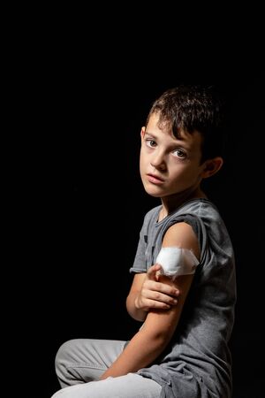 Cute little boy with sticking plaster on arm on black backgroundの写真素材