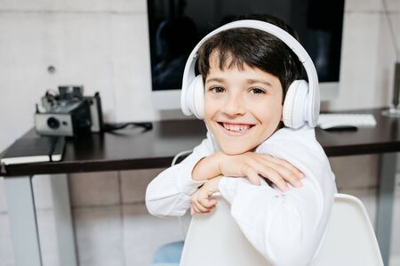 A little boy wearing a white shirt holding for a photo with white headphonesの写真素材