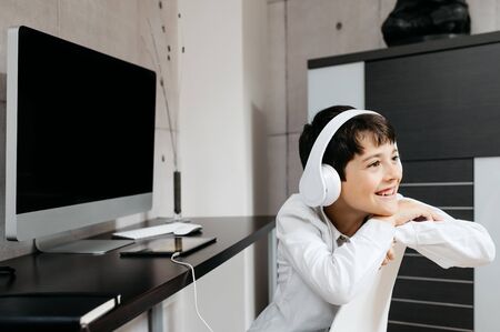 A little boy wearing a white shirt holding for a photo with white headphonesの写真素材