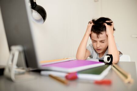 Stress kid doing homework.Boy at study table doing homework with stress action.Lazy boy doing homework with stressed face.の写真素材