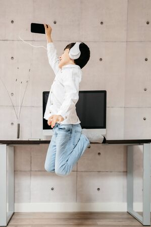 happy boy jumping with the phone in his hand and headphonesの写真素材