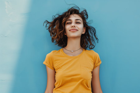 A woman in a yellow shirt is smiling and laying on a blue wall. Concept of relaxation and happinessの素材