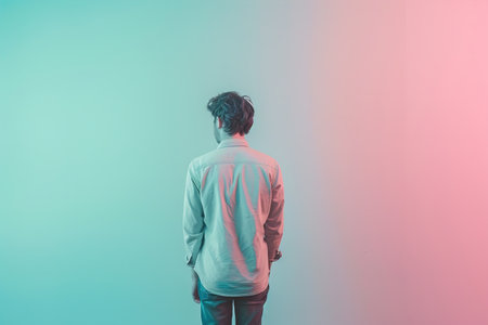 A man is standing in front of a wall with a pinkish blue background. He is wearing a white shirt and jeansの素材