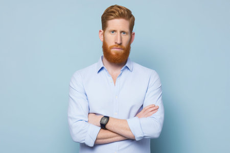 A man with a beard and a watch is standing with his arms crossed. He looks serious and focusedの素材