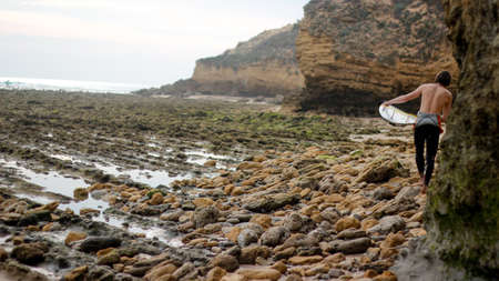 surfer walking through the rocks on the sea sideの写真素材