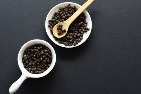 (Piper nigrum) Black pepper seeds, displayed in containers on wooden backgroundの写真素材