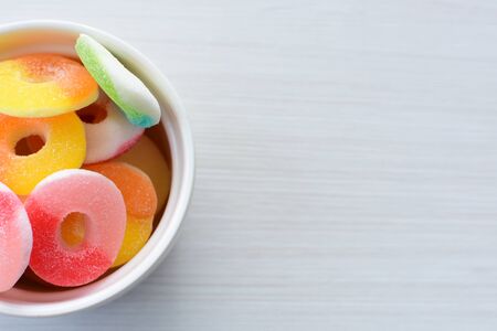Multicolored candy jelly beans, red, yellow, green, blue displayed in containers on white wooden backgroundの写真素材