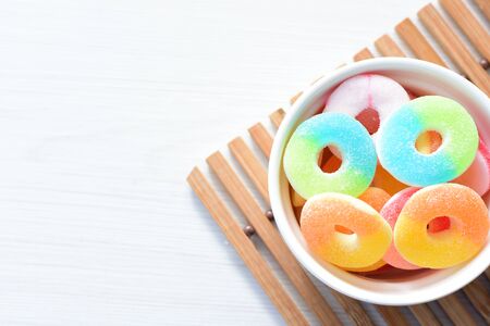 Multicolored candy jelly beans, red, yellow, green, blue displayed in containers on white wooden backgroundの写真素材