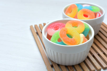 Multicolored candy jelly beans, red, yellow, green, blue displayed in containers on white wooden backgroundの写真素材