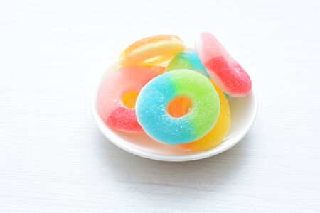 Multicolored candy jelly beans, red, yellow, green, blue displayed in containers on white wooden backgroundの写真素材