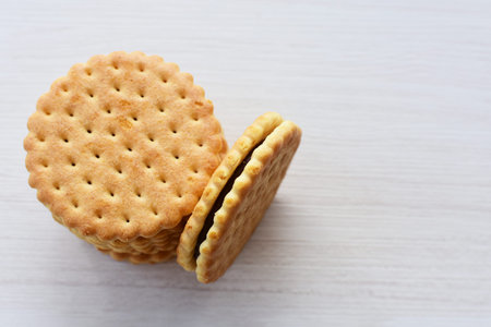 Double small vanilla cookies, with chocolate cream inside, open and closed cookies on white wooden...
