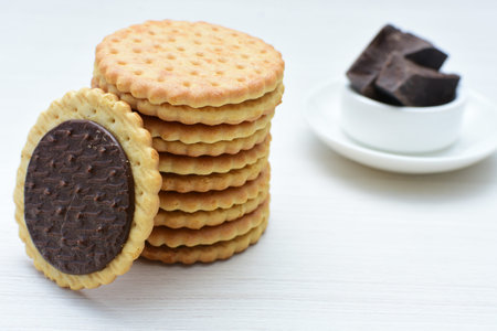 Double small vanilla cookies, with chocolate cream inside, open and closed cookies on white wooden...