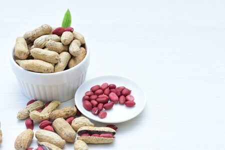 Arachis hypogaea - groundnut, whole, displayed in containers on white wooden backgroundの写真素材