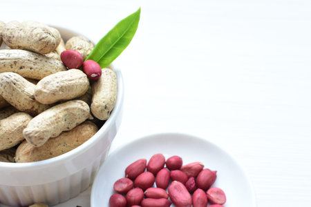 Arachis hypogaea - groundnut, whole, displayed in containers on white wooden background