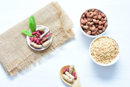 Arachis hypogaea - groundnut, whole, displayed in containers on white wooden background