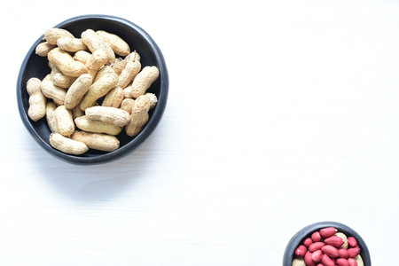 Arachis hypogaea - groundnut, whole, displayed in containers on white wooden background