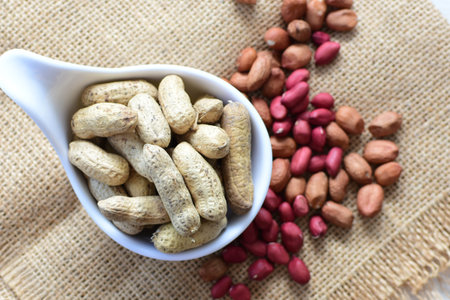 Arachis hypogaea - groundnut, whole, displayed in containers on white wooden background