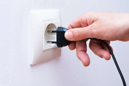Plugging a black electrical plug into a wall socket with a womans hand.の写真素材