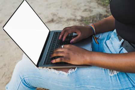 Close-up of African American womans hands using laptop computer, sitting on park bench. Mockup.の写真素材