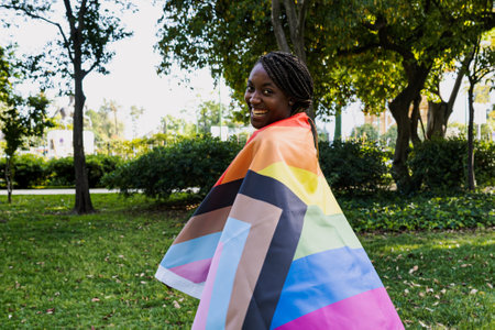 A smiling black woman has fun wrapping herself in the lgtb flag on Pride Day.の写真素材