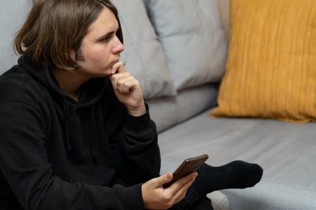 Young man with serious gesture who is thoughtfully holding a smart phone.