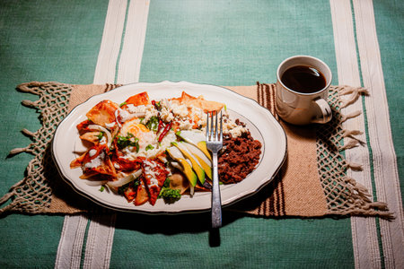 A chilaquiles Mexican food with in red sauce, cheese, cream, chili peppers on vintage background and coffeeの写真素材