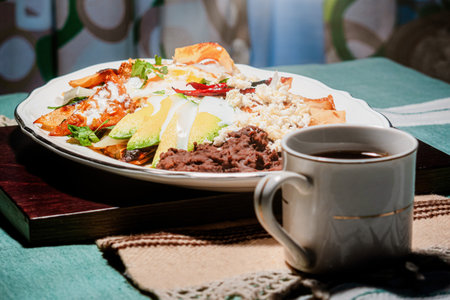 A chilaquiles Mexican food with in red sauce, cheese, cream, chili peppers on vintage background and coffeeの写真素材