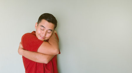 A young man hugging himself, in love, smiling, staying singleの写真素材