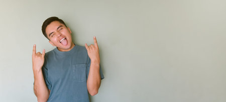 A young man making rock and roll sign and sticking out his tongue