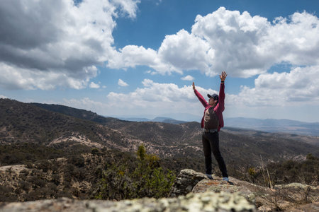 A man stands on top of a mountain with his arms raised in semi desert.の写真素材