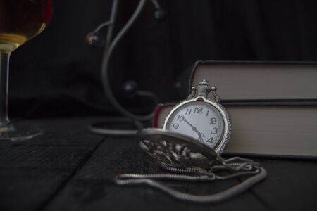 Pocket watch placed on some books. In the background is a glass of wine.の写真素材