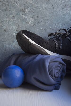 Black sneaker with white details and holes, a blue rolled towel and a blue foam rubber ball on a white base and a background in blue and gray tones.の写真素材