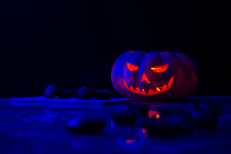 Halloween pumpkin with some out of focus pumpkin muffins in the foreground and more muffins on a wooden board next to it, all on a dark background.の写真素材