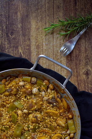 Valencian paella on cloth, with a fork and a sprig of rosemary on a wooden table, vertical.の写真素材