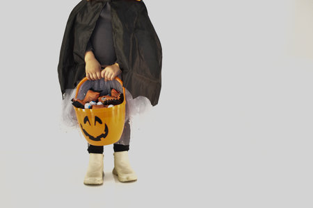 Little girl dressed as a witch holding her Halloween basket full of sweets, white background.の写真素材